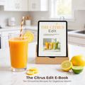 Glass of citrus smoothie with lemon slices beside a tablet showing 'The Citrus Edit' recipes on a kitchen counter.